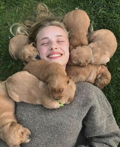 a woman laying in the grass with puppies on her shoulders and smiling at the camera