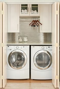 a washer and dryer in a small room with white cupboards above them