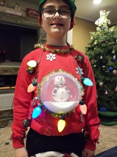 a young boy wearing a christmas sweater with lights around him and a snow globe in the middle