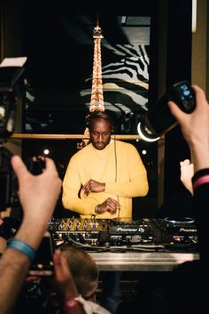 a man in a yellow shirt and headphones is surrounded by people at a dj booth