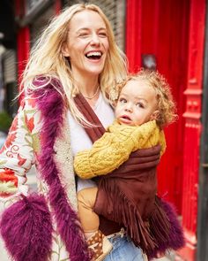 a woman holding a child in her arms and smiling at the camera while walking down the street