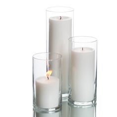 three white candles sitting in glass vases with one lit and the other half empty