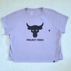 Brand New With Tags Under Armour X Project Rock Bull Head Logo Tee Size Large Approx Measurements Laying Flat: Length 24" Armpit To Armpit 25.5" Across Bottom Hem 25.5" 60% Cotton 40% Polyester Color Of Tee Is Lilac With A Graphic On Front Of A Slightly Distressed Bull's Head And "Project Rock" Below It Unique Curved Back Seam, Loose Fit, Crew Neckline, Short Sleeves, Straight Front Hem With Side Cutouts, Slightly Curved Back Hem, Black Under Armour Logo Tag On Front Left Bottom Hem, Incredibly Under Armour Graphic Print Tops For Streetwear, Bull Head Logo, Dwayne The Rock Johnson, Under Armour Logo, Bull Head, Rock Johnson, The Rock Dwayne Johnson, Dwayne The Rock, Curved Back