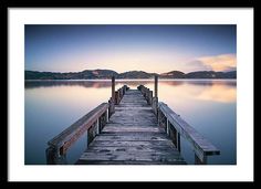 a wooden dock sitting on top of a body of water at sunset with mountains in the background