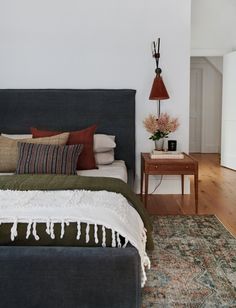 a bedroom with a bed, nightstand and lamp on the side table in front of it