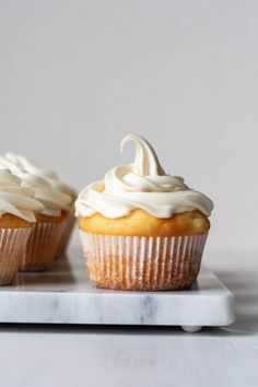 two cupcakes with white frosting on a marble tray