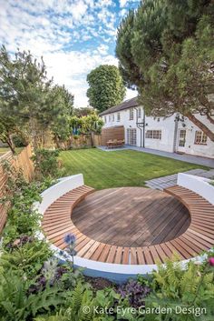 a circular wooden deck in the middle of a yard with trees and flowers around it