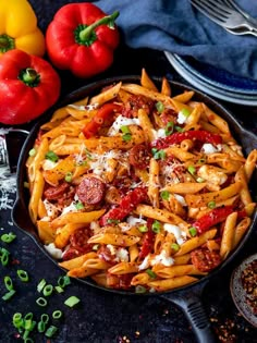 a skillet filled with pasta and vegetables on top of a black table next to some bread