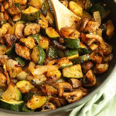 a skillet filled with cooked vegetables on top of a green cloth next to a wooden spoon