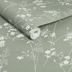 a green wallpaper with white flowers and leaves on the side, it has a roll of toilet paper in front of it