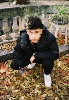 a young man sitting on top of leaves next to a bench