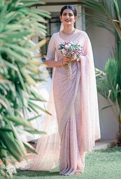 a woman wearing a pink sari and holding a bouquet in front of some palm trees