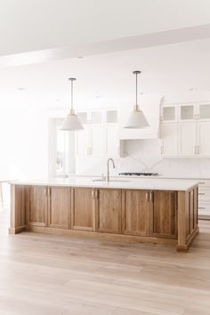 an empty kitchen with white cabinets and wooden flooring is pictured in this image, there are two pendant lights hanging over the island