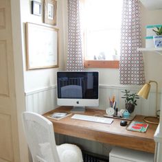 a desk with a computer on top of it next to a white chair and window