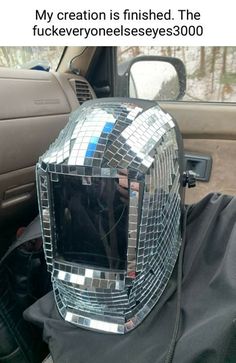 a person in a car with a helmet made out of mirrored tiles on the hood