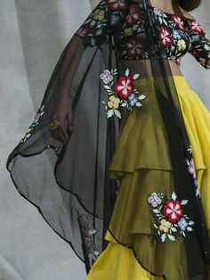 This vibrant set features a black off shoulder blouse in silk and net base with cutdana and multi-coloured thread hand embroidered floral motifs. It is paired with a yellow ruffles tiered lehenga skirt and a black net dupatta. Summer Organza Sharara With Sheer Dupatta, Yellow Organza Sharara With Intricate Embroidery, Yellow Sharara With Floral Embroidery For Party, Yellow Floral Embroidery Sharara For Party, Yellow Floral Embroidered Sharara For Party, Spring Multicolor Choli With Dupatta, Yellow Lehenga With Floral Embroidery For Party, Spring Choli With Sheer Dupatta In Georgette, Spring Georgette Choli With Sheer Dupatta