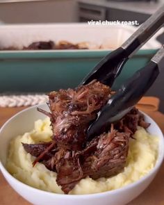 a white bowl filled with meat and mashed potatoes on top of a wooden table