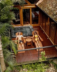 two people in bathing suits sitting on wooden chairs next to an outdoor jacuzzi