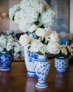 three blue and white vases with flowers in them on a wooden table next to each other