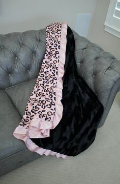 a black and pink leopard print blanket sitting on top of a gray couch next to a window