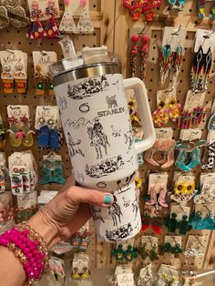 a person holding up a coffee mug in front of a wall full of earring hooks