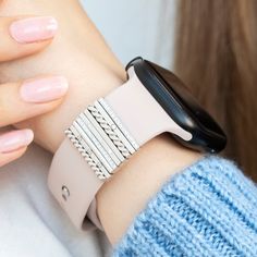 a woman wearing a smart watch on her arm with pink nail polishes and a blue sweater