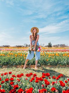 a woman standing in a field full of red and yellow flowers with a hat on