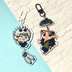 two keychains with anime characters on them sitting on a blue and white surface