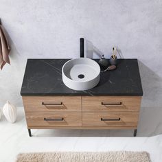 a bathroom vanity with black marble counter top and wooden drawers, along with a white rug on the floor