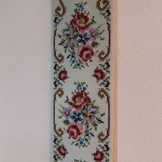 a cross stitched wall hanging on the side of a white wall with red and blue flowers