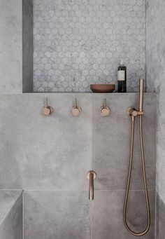 a bathroom with grey tiles and gold faucets on the shower head, two soap dispensers in the background