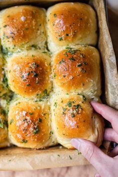 a person holding a tray full of bread rolls with cheese and herbs on top, ready to be baked