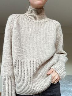 a woman standing in front of a bed wearing a turtle neck sweater