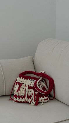 a red and white purse sitting on the back of a couch next to a pillow