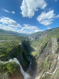 an aerial view of a waterfall with a rainbow in the middle and mountains behind it