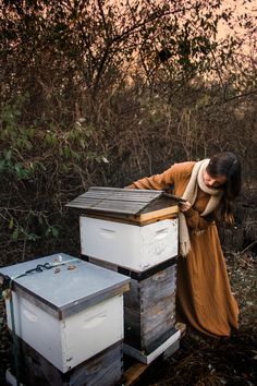 a woman leaning over some beehives in the woods