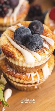 some pancakes with blueberries and cream on top are sitting on a wooden table next to berries