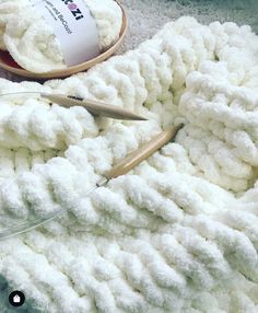 there is a white crochet blanket next to some knitting needles