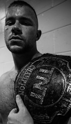 a shirtless man holding a wrestling belt in front of his face and looking at the camera