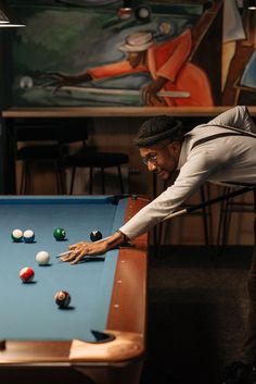 a man leaning over a pool table to pick up balls with his arm and hand