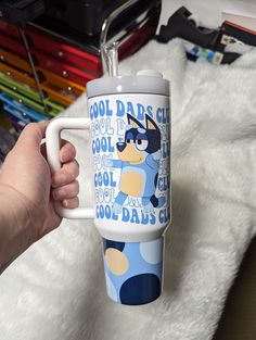 a person holding a coffee mug with the words cool dads club on it in front of a pile of other items