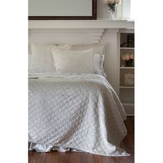 a bed with white comforter and pillows in front of a mirror on the wall