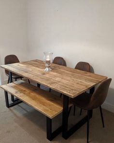 a wooden table with four chairs and a bench in front of it, against a white wall