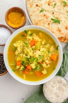 a bowl of chicken soup next to two bowls of rice, bread and other ingredients