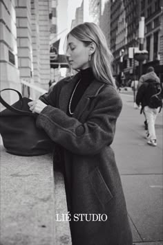 a woman leaning against a wall with her hand on the purse and looking at it