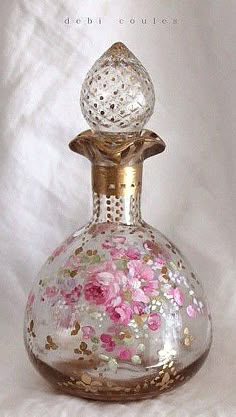 a glass bottle with pink flowers painted on the inside and gold trimming around it