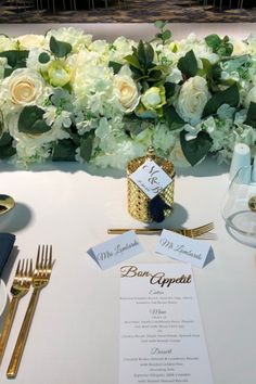 the table is set with white flowers and gold place settings for an elegant wedding reception