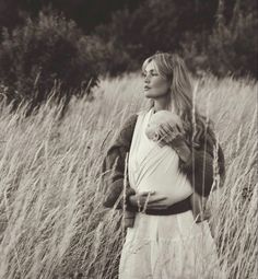 a woman standing in tall grass holding a baby