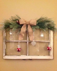 an old window decorated with christmas ornaments and greenery is hung on the wall by a bow