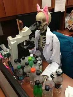 a skeleton is looking through a microscope with bottles on the table in front of it